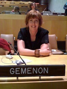 A woman in a conference chamber at the UN behind a sign that says Gemenon.