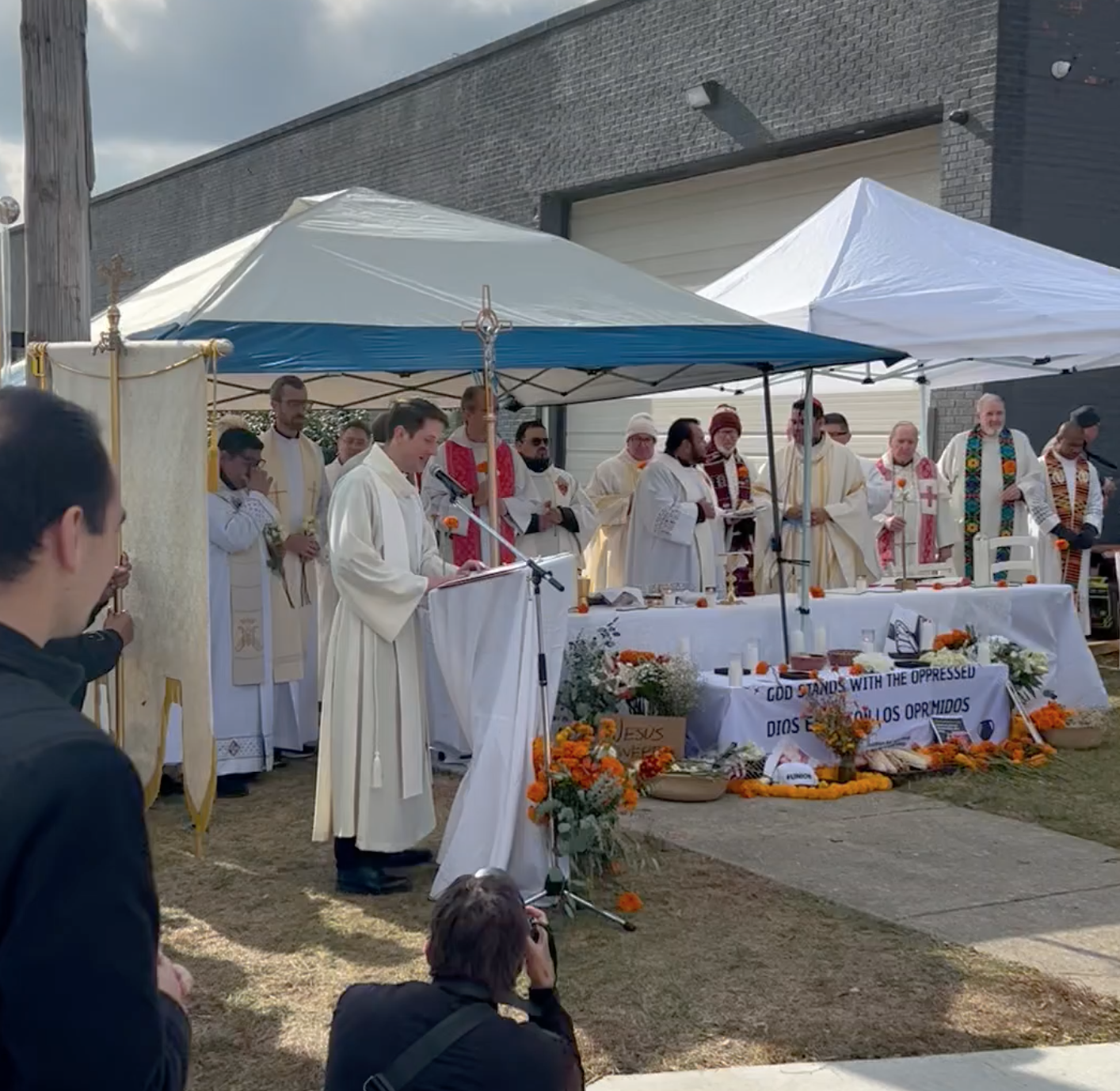 More than a dozen priests and clergy under tents outside Broadview ICE offer a religious service and one speaks into a microphone.
