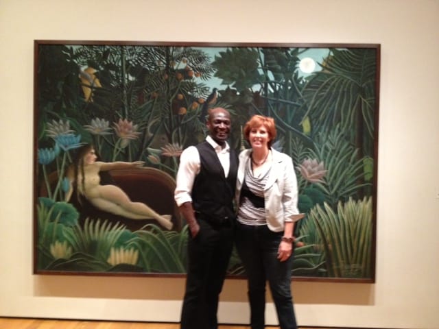 Peter Mensah and Mo Ryan in front of a painting of a woman reclining amid a tropical forest